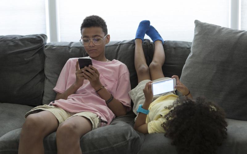 Two kids with phones in their hand laying and sitting on the couch