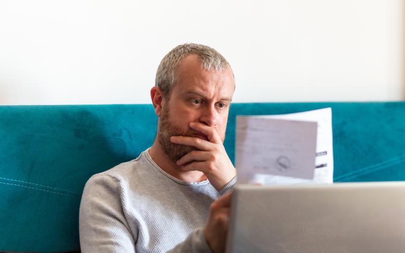 Man van middelbare leeftijd zit op de bank en heeft een brief vast. Hij kijkt er zorgelijk naar.