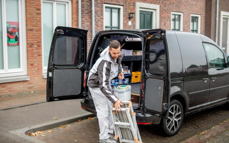 Jongvolwassen man, een schilder, staat met zijn werkspullen bij zijn bus. Hij is aan het uitladen.