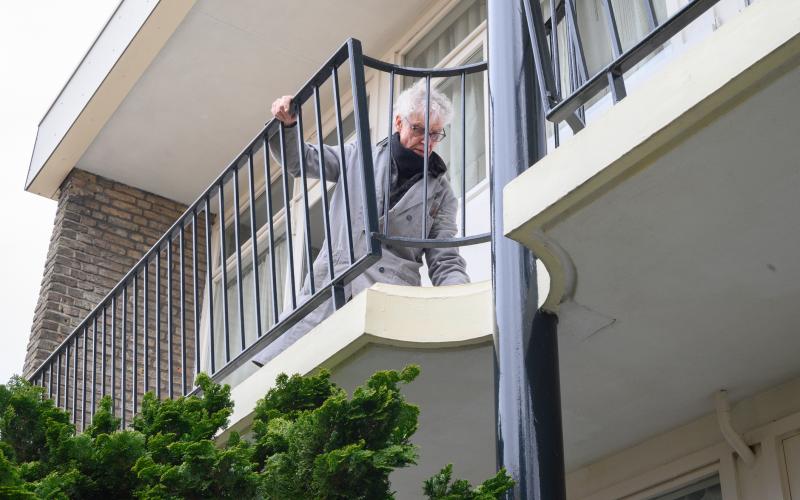 Oudere man houdt trailiewerk vast bij appartement 