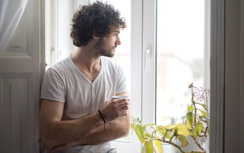 Man met koffie in hand kijkt uit zijn raam