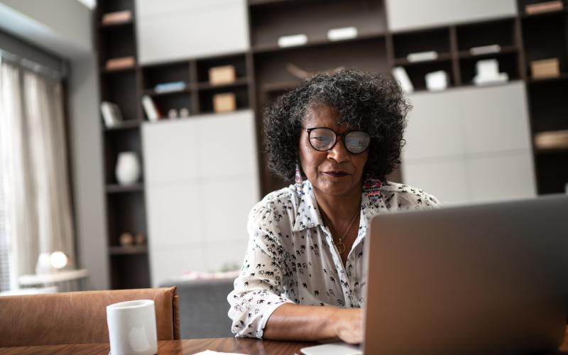 Vrouw zit achter laptop. Ze heeft krullend haar en draagt een bril