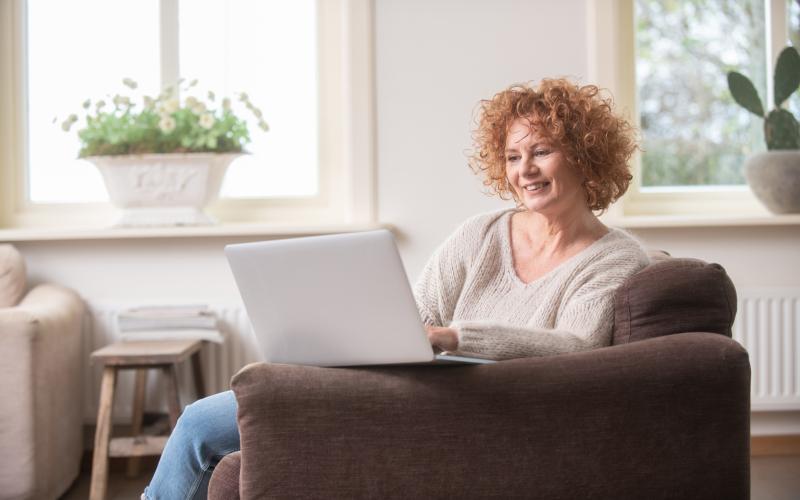 Vrouw met rood krullend haar zit op de bank en heeft haar laptop voor zich