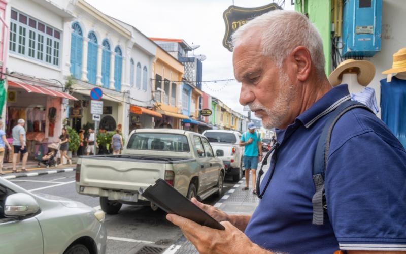 Senior man in Thailand. Hij kijkt op zijn telefoon.