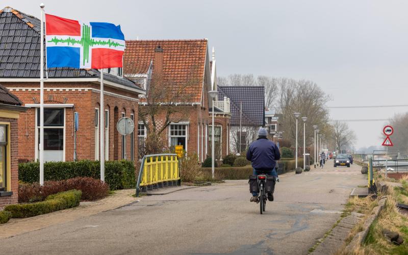 Een man op een gemotoriseerde fiets rijdt langs een aantal huizen in de provincie Groningen