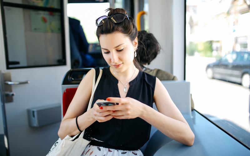 Witte vrouw zit in de tram. Ze kijkt op haar telefoon.