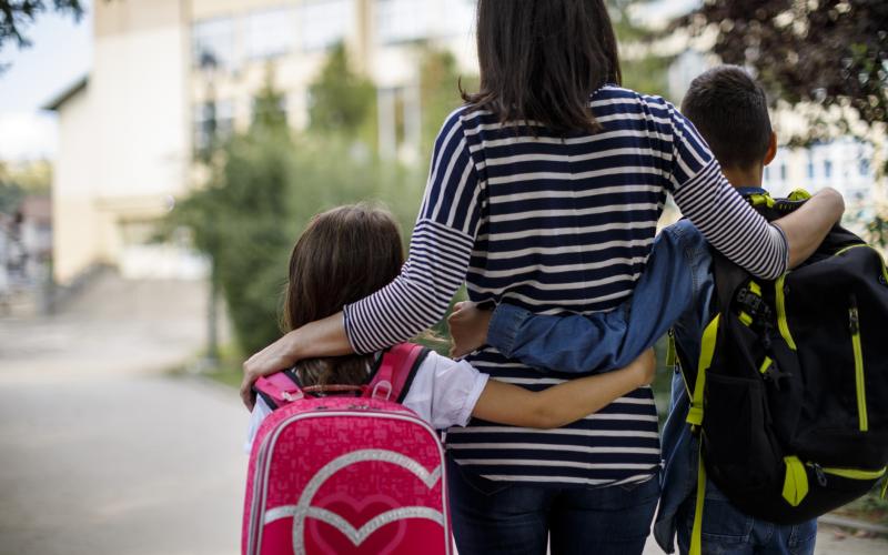 Moeder met twee kinderen van achteren gefotografeerd. Ze omhelzen elkaar.