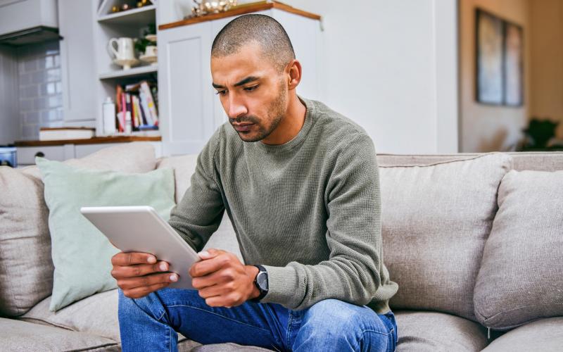 Man zit op de bank en kijkt serieus naar zijn tablet