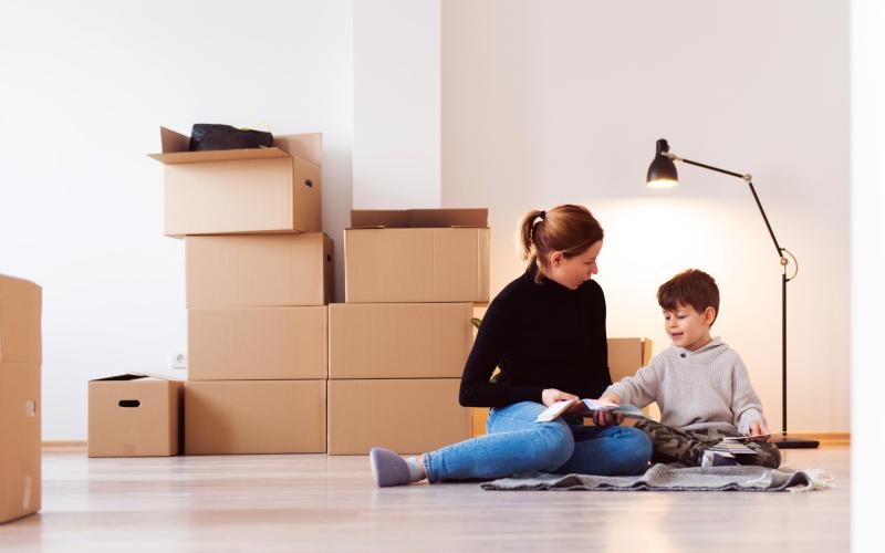 Moeder en zoon zitten op de grond in kamer. Op de grond staan verhuisdozen