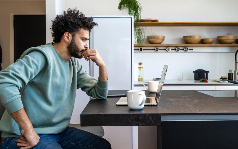 Man met krullend haar zit aan keukentafel achter een laptop