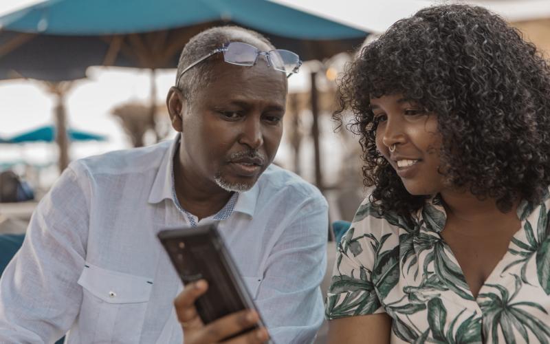 Oudere man met kleindochter op een strandterras. Ze kijken beiden naar een telefoon