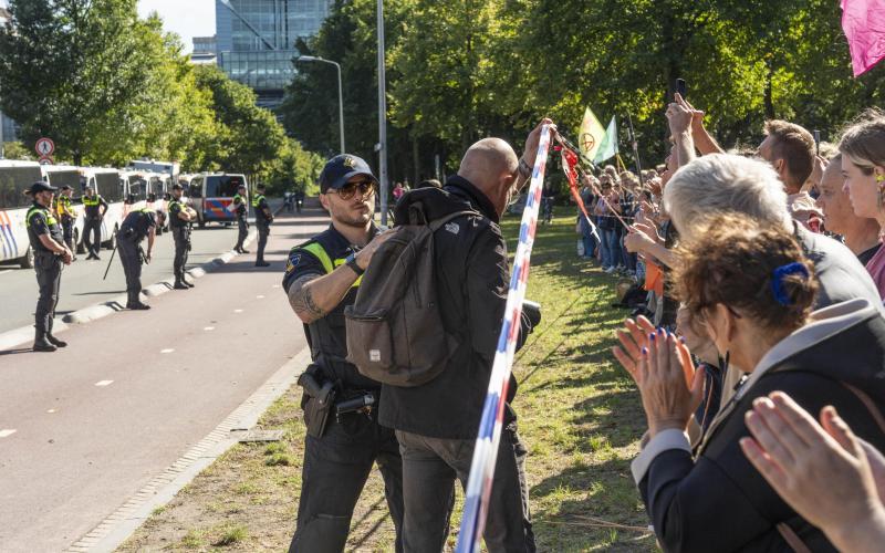 Een politieagent duwt een journalist achter een politielint