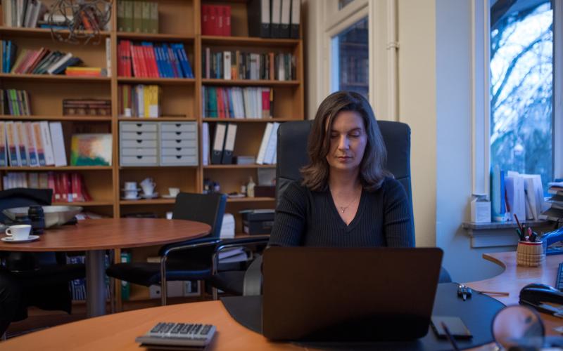 Vrouw van middelbare leeftijd zit thuis achter een bureau met een laptop