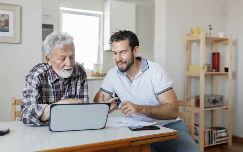 Man helpt senior man met het regelen van zaken. Ze kijken samen naar de papieren en een laptop.