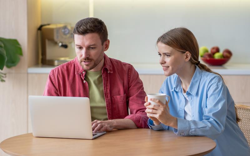 Een stel (man en vrouw) zitten samen aan de keukentafel en kijken naar een laptop