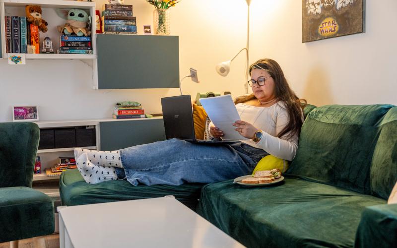 Jonge vrouw zit thuis op de bank en heeft papieren in haar hand