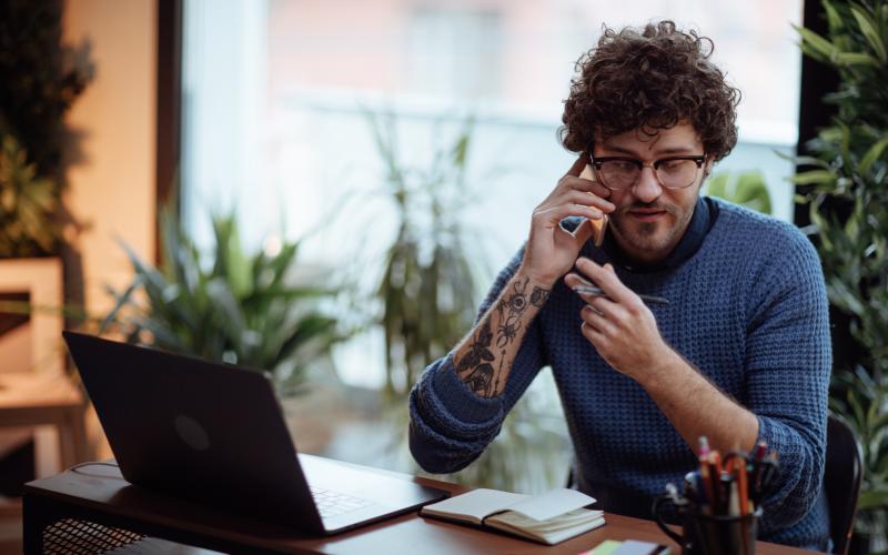 Een jonge ondernemer zit achter zijn laptop en belt met iemand