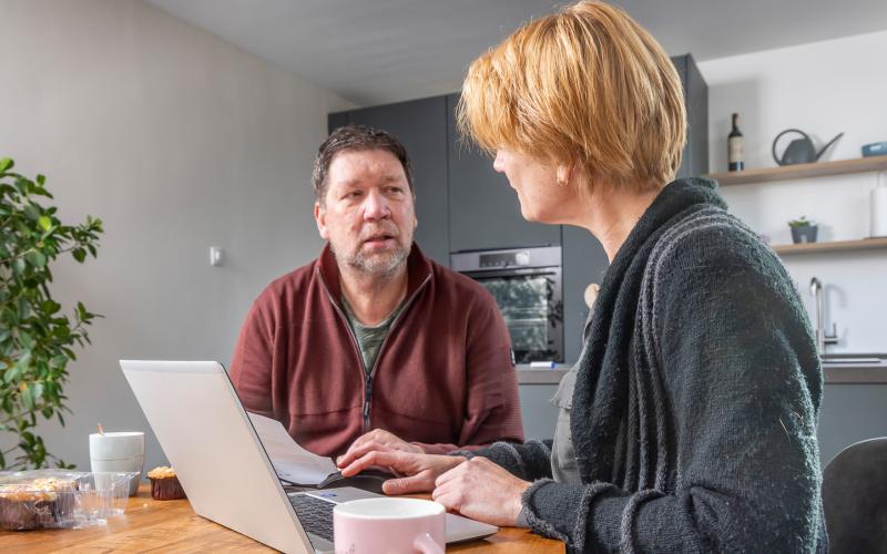 Man en vrouw thuis aan tafel met laptop en papieren voor zich.