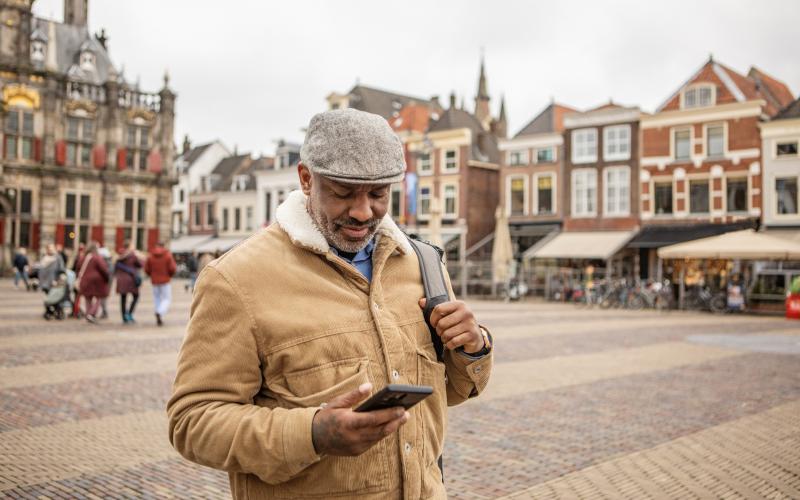 Een oudere man (55) staat op een plein in de binnenstad van Delft met een telefoon in zijn hand