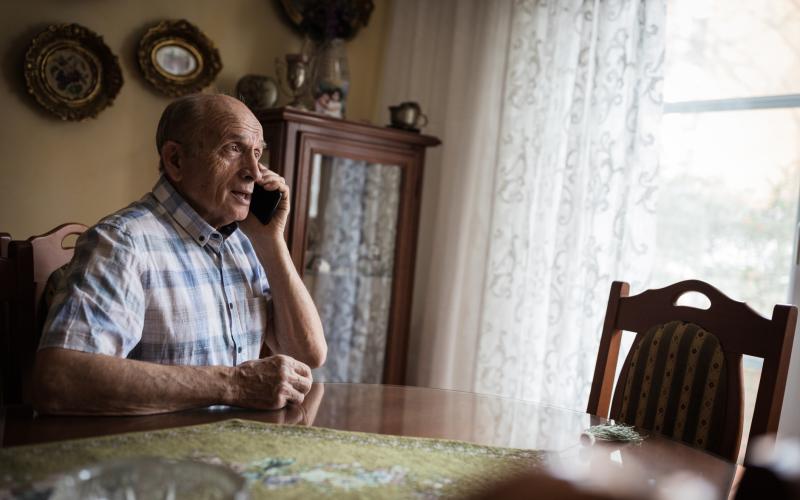 Oudere man zit aan zijn tafel en is aan het bellen