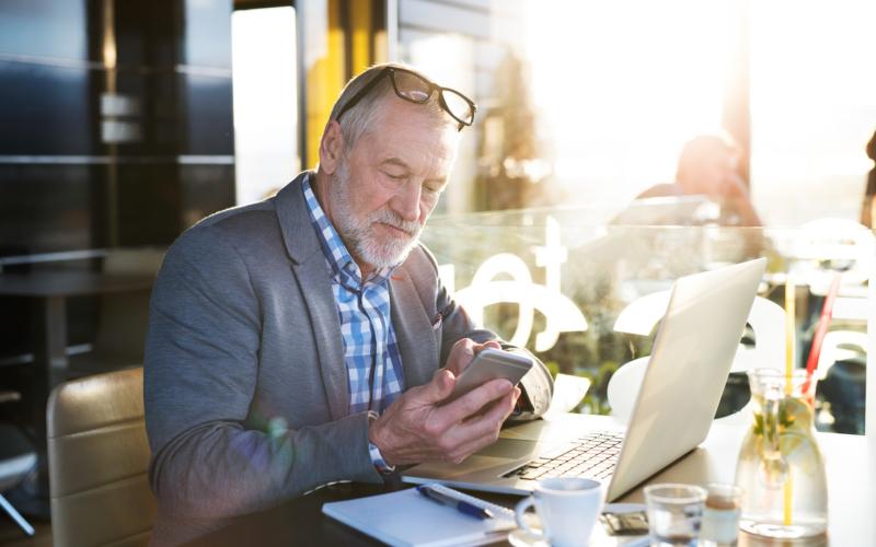 Senior man zit te werken en achter zijn laptop