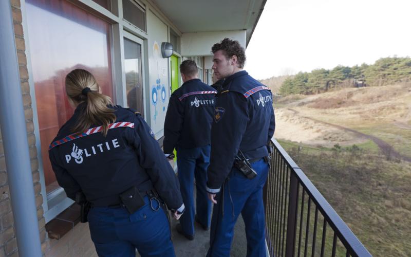 Drie politieagenten voor een woning, natuur op de achtergrond