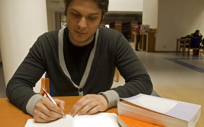 Man maakt inburgeringsexamen aan tafel met stapel boeken ernaast