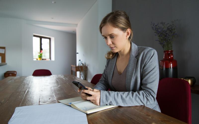 Jonge vrouw met mobiel aan de tafel