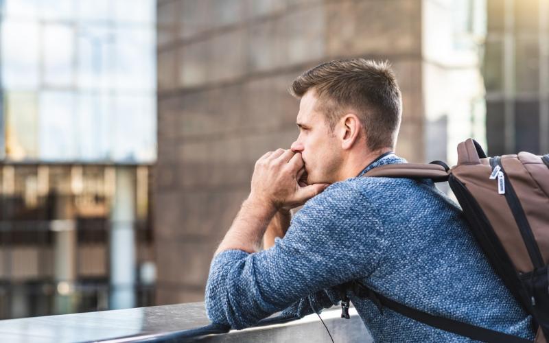 Jongeman met rugzak op rug houdt handen onder kin