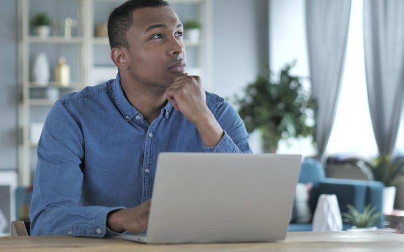 Man zit achter zijn laptop en kijkt bedenkend omhoog