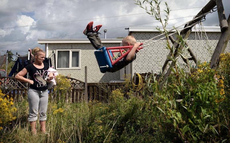 vrouw kijkt naar schommelend kind in tuin