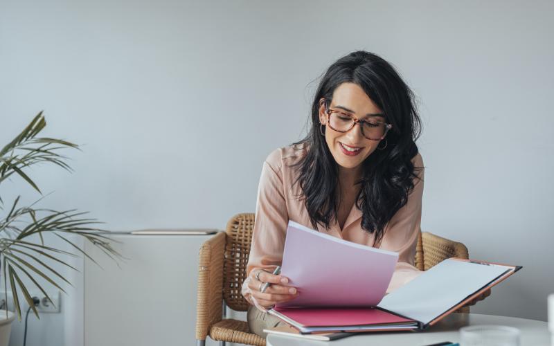 Vrouw met lang donker haar, donkere bril en roze blouse leest folders