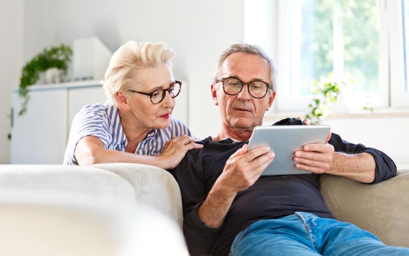 Ouder stel zit op de bank met iPad in de hand