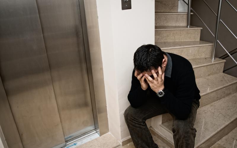 Man zit in trappenhuis met handen voor gezicht en in het haar