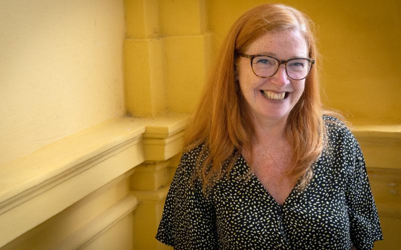 Lachende vrouw (mantelzorger Ingrid Keestra) met lang rood haar, een bril en draagt een zwart shirt