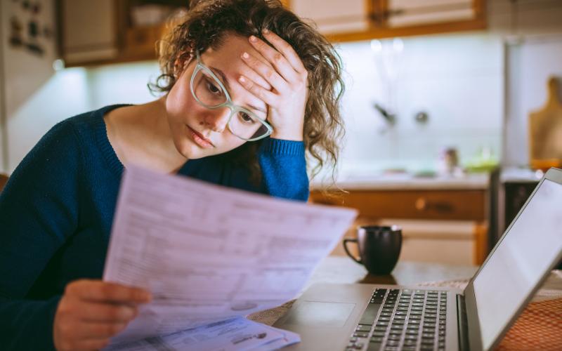 Vrouw zit achter de laptop en kijkt bezorgd naar een brief in haar handen