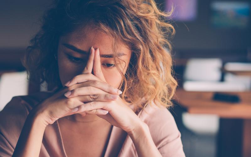 Jonge vrouw leunt met haar hoofd op haar handen die ze gevouwen voor zich houdt