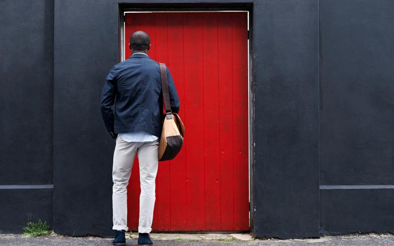 Man met tas, op de rug gezien, staat voor dichte rode deur