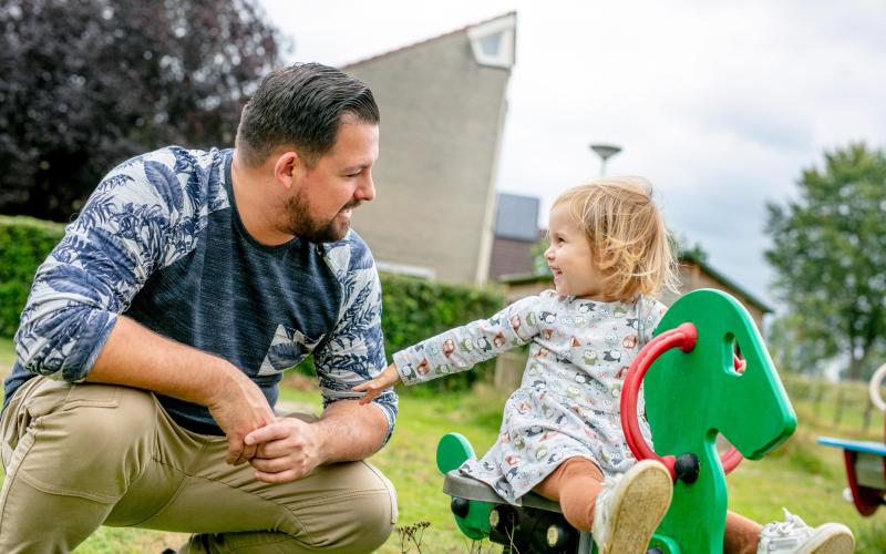 Jonge ouder man met zijn dochtertje in de speeltuin. Dochtertje zit op wipwap.