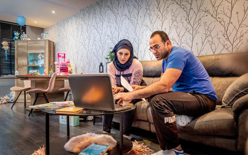 Man en vrouw zitten thuis op de bank. Voor zich hebben zij een laptop en in de hand papieren.