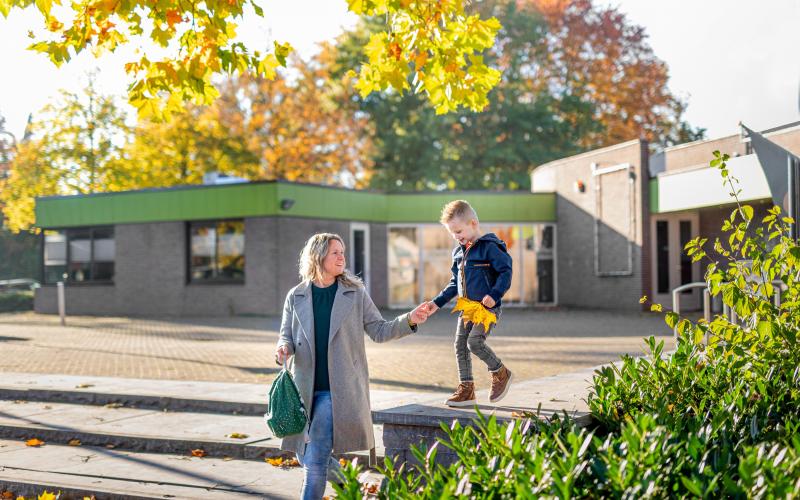 Moeder loopt hand in hand met haar zoontje voor een openbaar gebouw