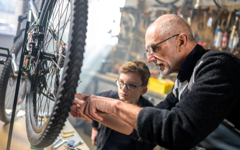 Een opa en zijn kleinzoon reparen een fiets, deze is zichtbaar in beeld.