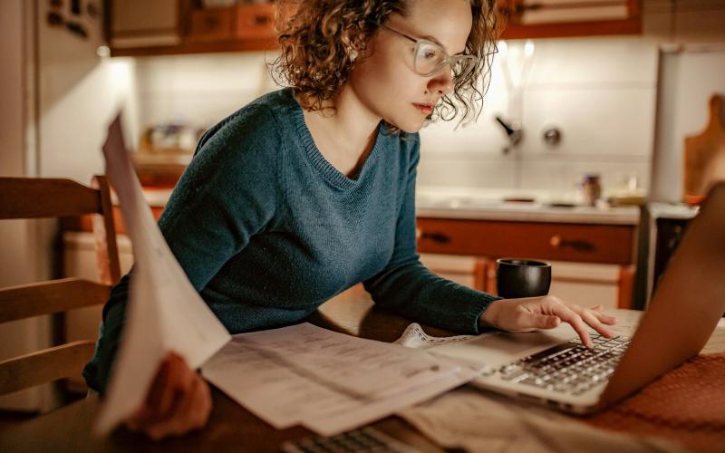 Jonge vrouw achter de computer met rekeningen in haar hand