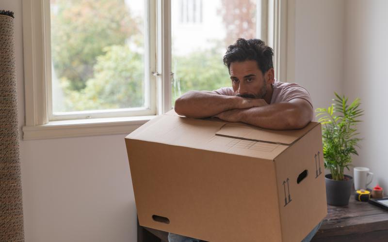 Man zit met een verhuisdoos op zijn schoot. Hij kijkt vertwijfeld voor zich uit.