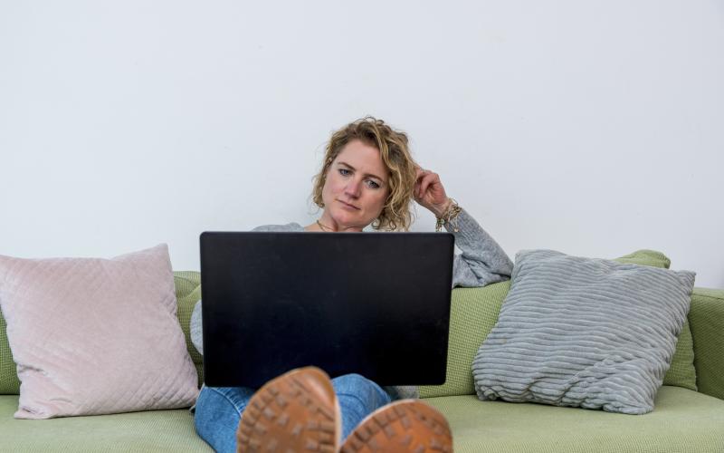 Een vrouw van middelbare leeftijd zit met een laptop op de bank