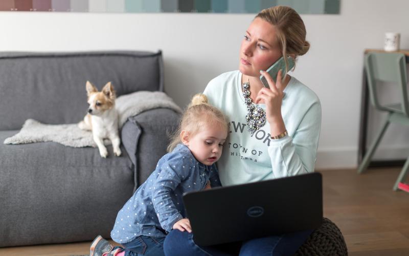 Een vrouw aan de telefoon met kind op schoot