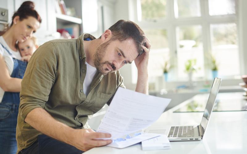 Man, zittend in keuken, kijkt bezorgd naar document in zijn hand