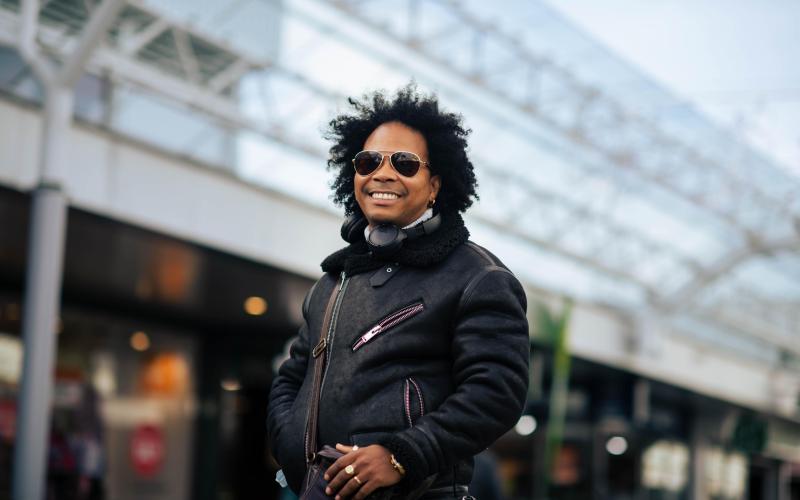 Man (Michel) met zonnebril staat in winkelstraat en kijkt lachend in de camera