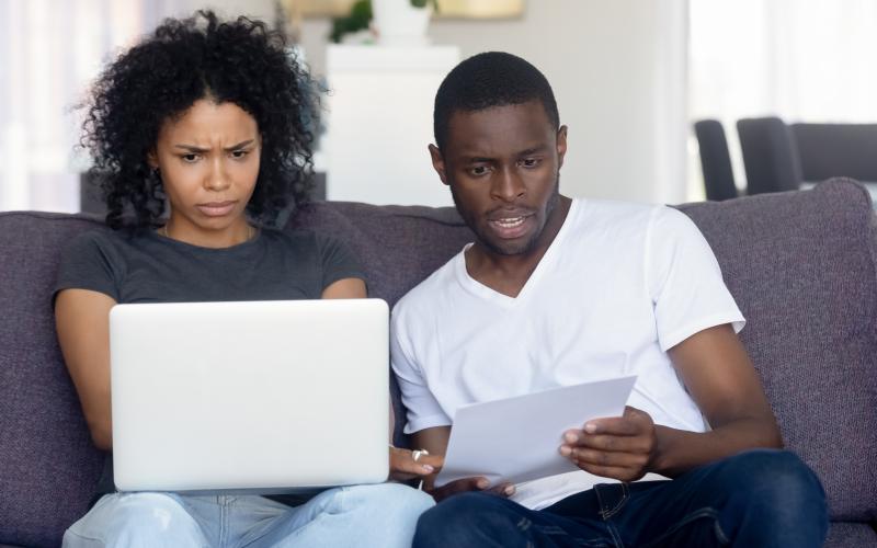 Echtpaar naast elkaar op de bank, kijkt verbaasd naar laptop