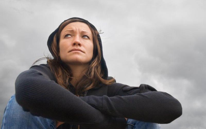 Zittende vrouw met zwarte trui en capuchon, de lucht is bewolkt 